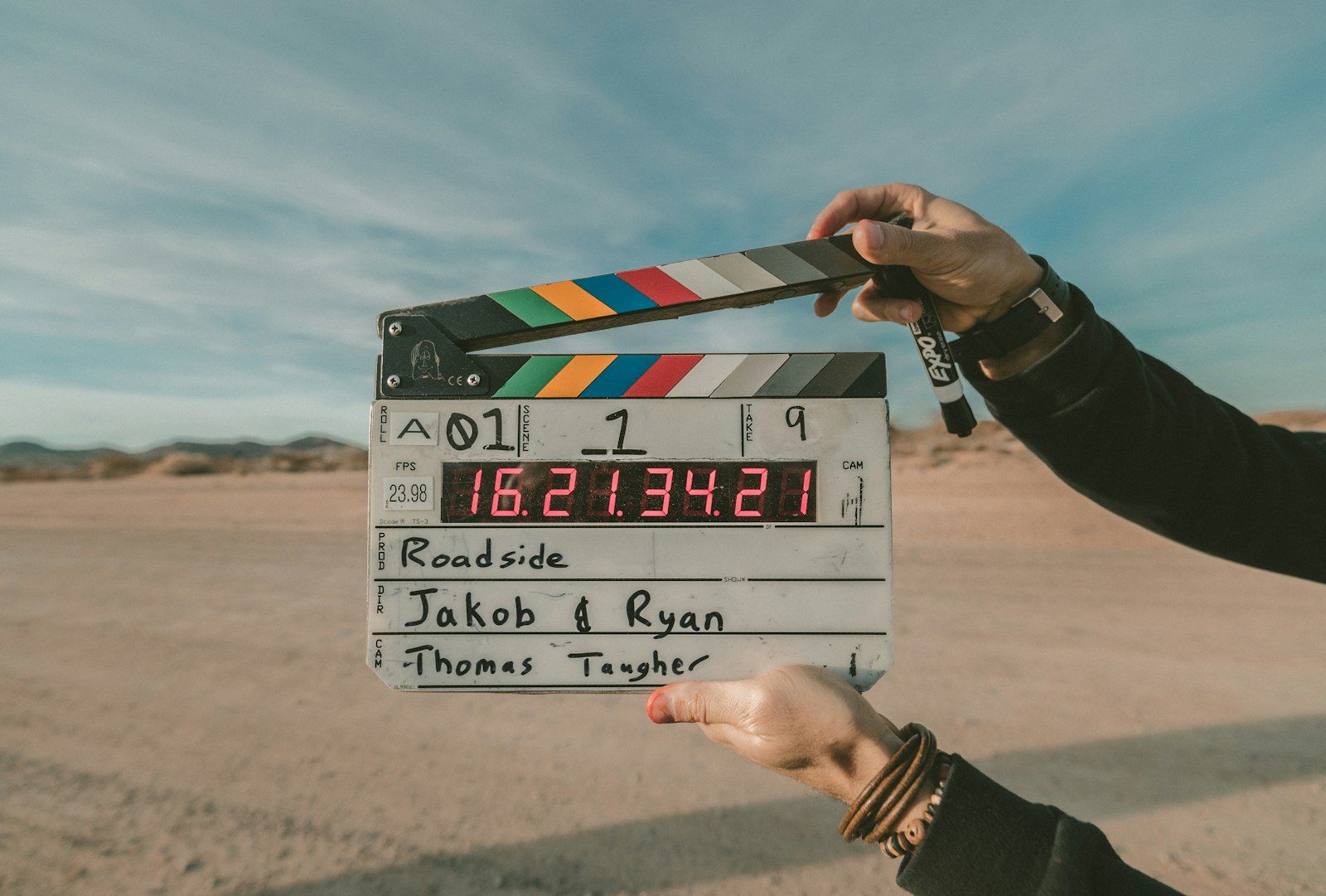 Two filmmakers holding a clapperboard on a desert roadside at golden hour