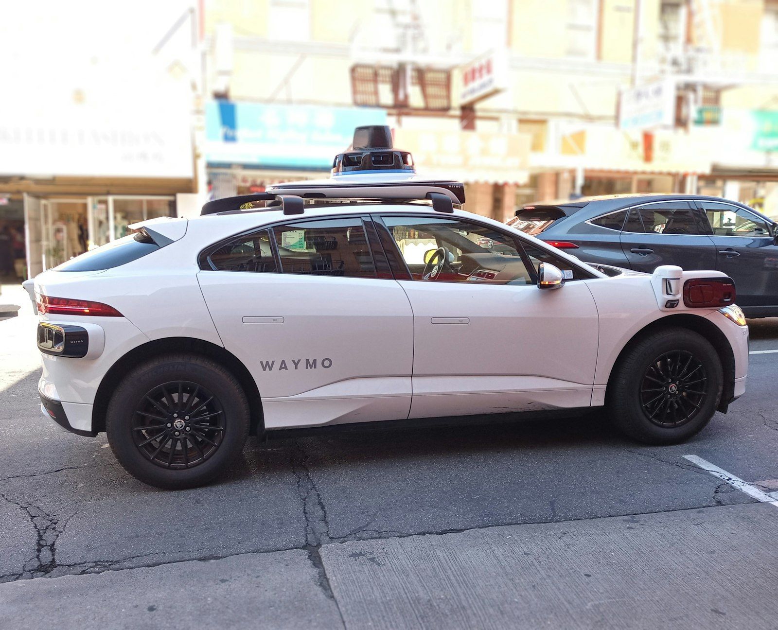White Waymo robotaxi with roof-mounted sensor dome driving through a city street